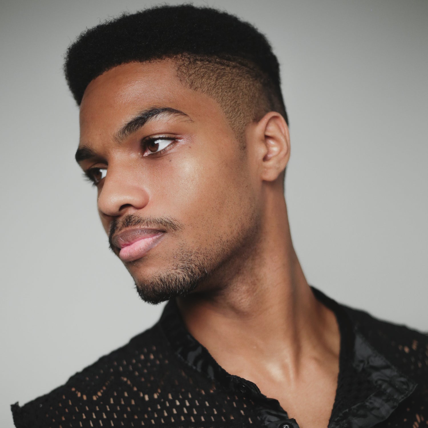 Man wearing a black sleeveless top with intricate patterns against a gray background