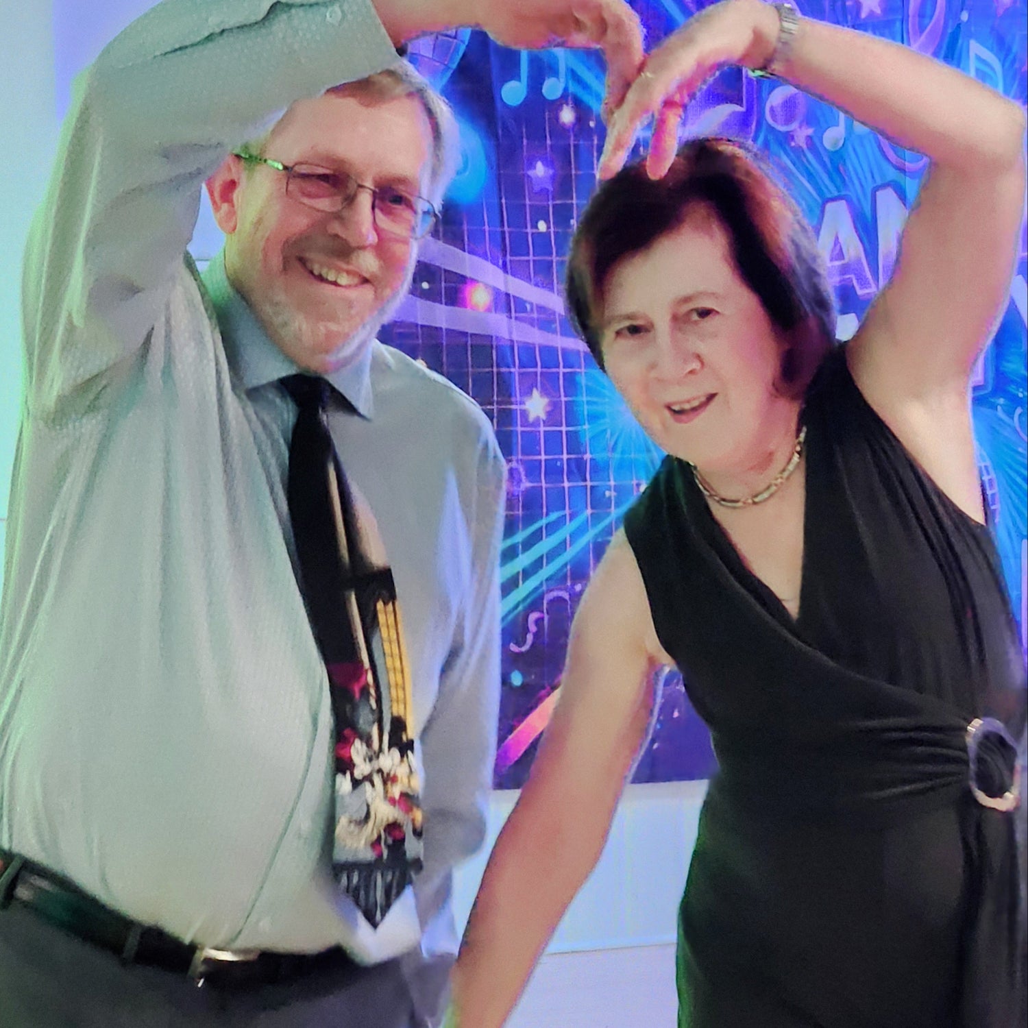 Two people posing with their hands above their heads in front of a colorful background.